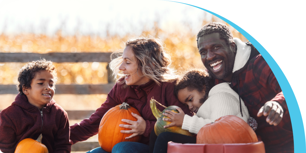 Family of four holding pumpkins laughing and smiling together