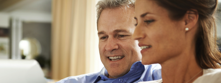 A man and a woman sitting on a couch looking at a tablet and talking