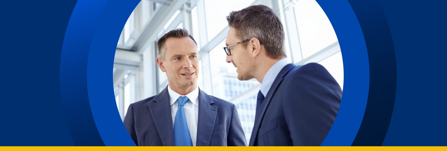 Two businessmen in an office standing and talking next to a window