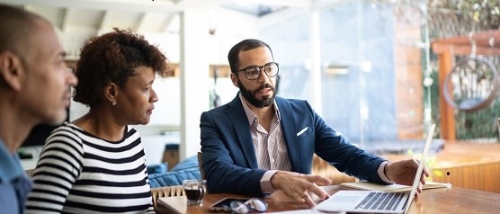 A man sitting in front of a laptop discussing with a man and a woman something on the laptop screen