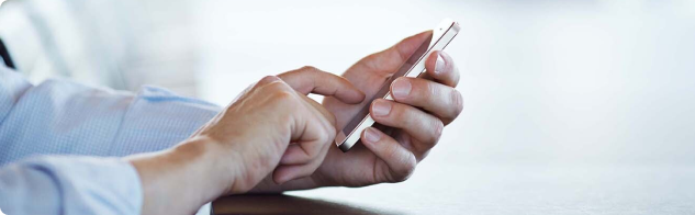 Man, wearing a blue dress shirt with sleeves rolled up, scrolling on a phone